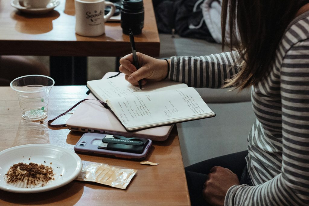 A woman writing in a notebook at a café table